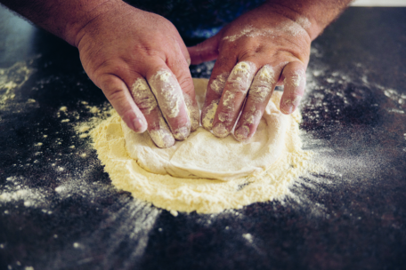 Die Hände drücken und formen den Teig auf einer dunklen, mit Mehl bestäubten Arbeitsfläche und bereiten ihn zum Backen vor.