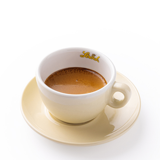 Eine beigefarbene Tasse mit Untertasse, die mit Espresso gefüllt ist und auf der sich eine Cremaschicht befindet. Die Tasse hat einen runden Henkel und ein kleines Logo mit dem Wort Simsek im Rand. Der Hintergrund ist weiß.