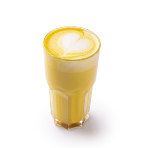 Ein Glas goldener Kurkuma-Latte mit einem herzförmigen Muster im Schaum vor einem weißen Hintergrund.