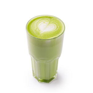 Ein klares Glas, gefüllt mit einem cremig-grünen Matcha-Latte, gekrönt von einem herzförmigen Latte-Art-Motiv aus weißem Schaum, vor weißem Hintergrund.