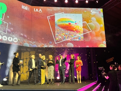 Eine Gruppe von Menschen steht bei einer Preisverleihung auf der Bühne, umgeben von Konfetti. Auf einer großen Leinwand hinter ihnen wird ein buntes Blasenbild angezeigt, auf dem "Effie Awards" und andere Logos zu sehen sind.