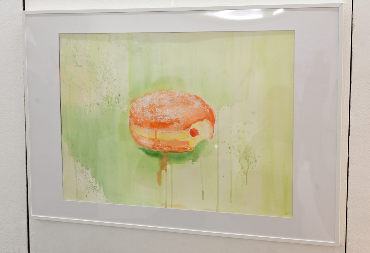 Gerahmte Aquarellmalerei eines mit Gelee gefüllten Donuts mit Puderzucker darauf, vor einem hellgrünen, abstrakten Hintergrund mit schwachen Farbtropfen.
