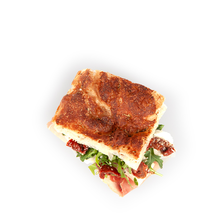 Ein quadratisches Sandwich aus Focaccia-Brot, gefüllt mit Rucola, sonnengetrockneten Tomaten und Pökelfleisch, von oben auf weißem Hintergrund fotografiert.