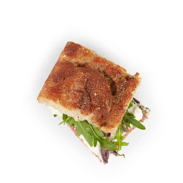 Ein quadratisches Sandwich auf rustikalem Focaccia-Brot, gefüllt mit frischem Rucola, cremigem Käse und Tomatenscheiben, von oben gesehen auf einem weißen Hintergrund.