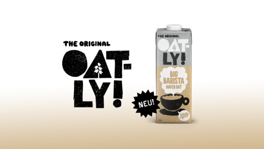 Ein 1-Liter-Hafermilchkarton von Oatly Barista steht aufrecht. Auf dem Etikett steht The Original Oatly! Bio Barista Hafer Oat mit einem Kaffeetassen-Symbol und NEU! in einem schwarzen Sternenhimmel. Der Hintergrund geht von Weiß zu Beige über.