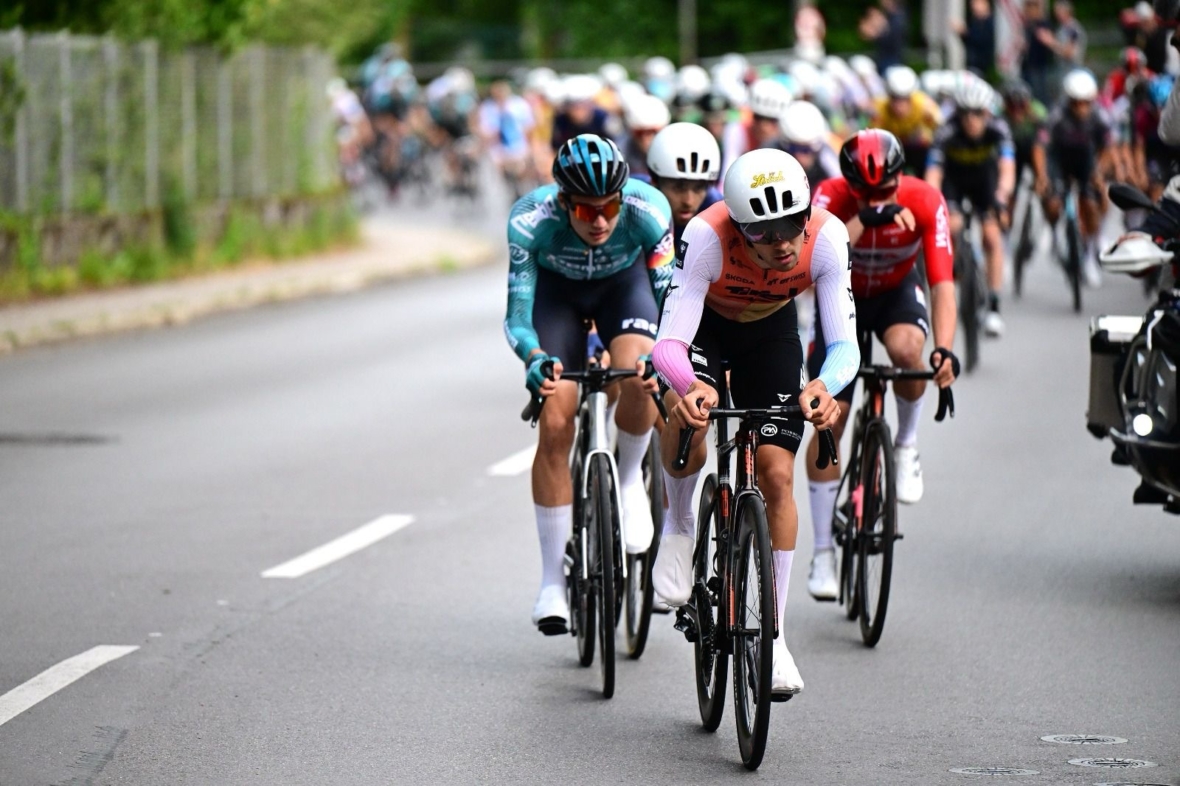 Eine Gruppe von Radfahrern in Rennkleidung und mit Helmen fährt während eines Radrennens eng zusammen auf einer Straße, mit unscharfen Fahrern im Hintergrund.