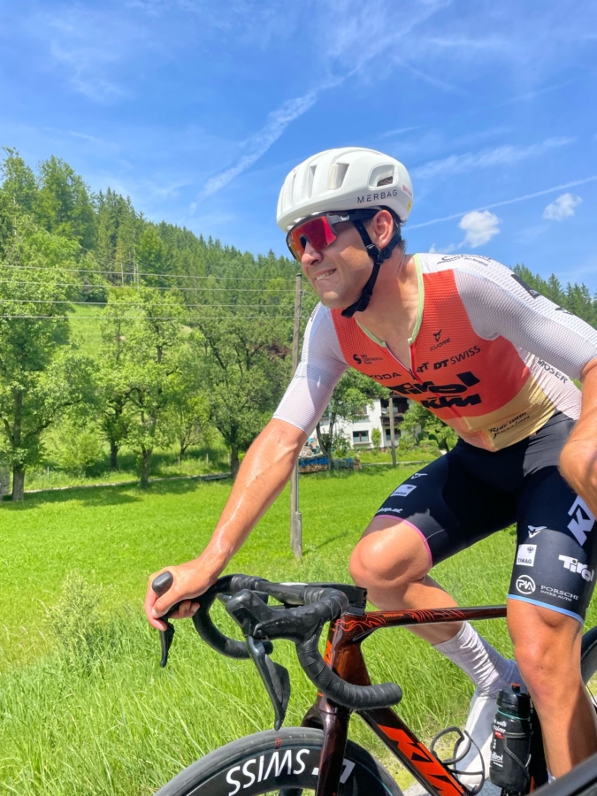 Ein Radfahrer, der einen weißen Helm, eine Sonnenbrille und eine Rennkleidung trägt, fährt an einem sonnigen Tag mit grünem Gras, Bäumen und blauem Himmel im Hintergrund im Freien Fahrrad.