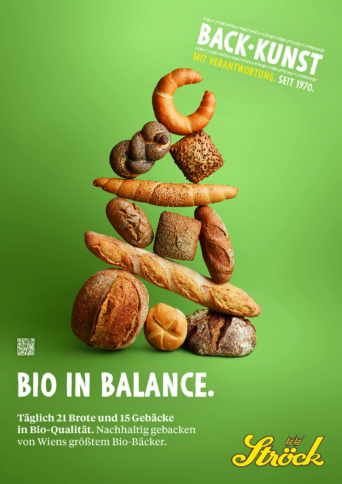 Eine Vielzahl von Broten und Brötchen sind kunstvoll in einem ausgewogenen Turm vor einem grünen Hintergrund gestapelt. Der Text hebt die Bio-Qualität und Nachhaltigkeit von Wiens größter Bio-Bäckerei Ströck hervor.