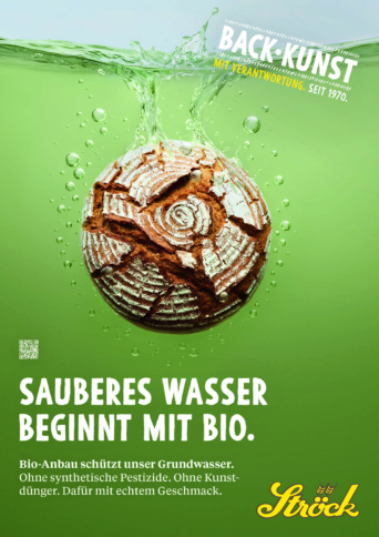 Ein runder Brotlaib mit einem Krustenmuster, das an plätscherndes Wasser erinnert, liegt auf einem grünen Hintergrund. Der deutsche Text wirbt für ökologischen Landbau und sauberes Wasser. Das Ströck-Logo erscheint unten rechts.
