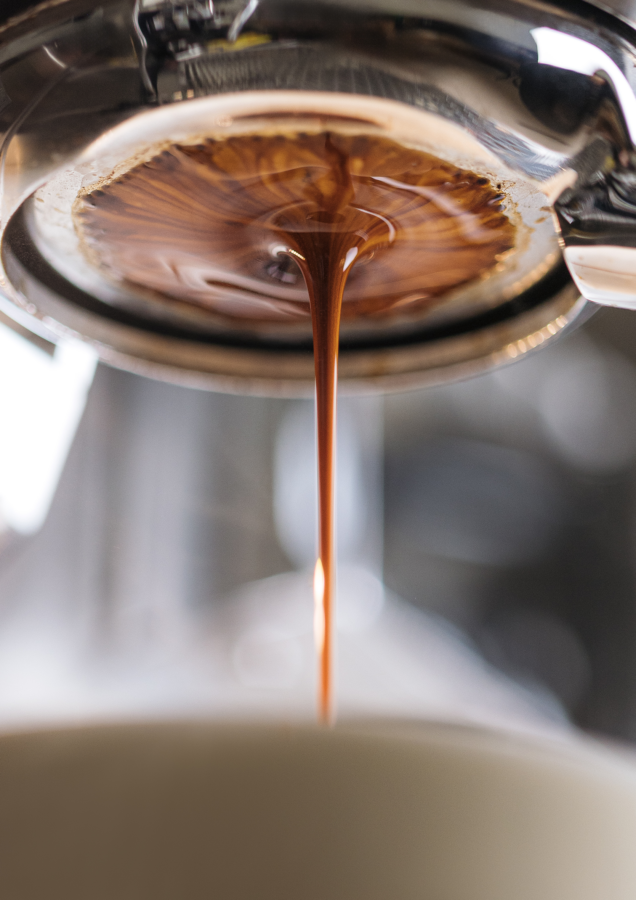 Ein gleichmäßiger Strahl dunklen Espressos fließt aus einem Siebträger in eine Tasse.