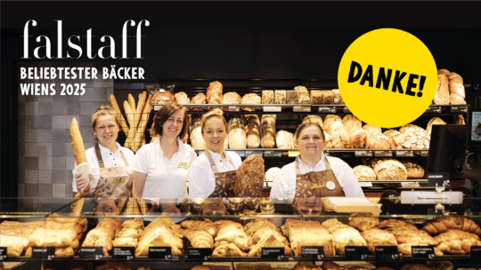 Vier lächelnde Bäckereimitarbeiter in Uniform stehen hinter einer Auslage mit verschiedenen Brotsorten und Gebäck. Rechts ist ein gelber Kreis mit der Aufschrift "DANKE!" zu sehen, darüber der Text: "falstaff beliebtester bäcker Wiens 2025.".