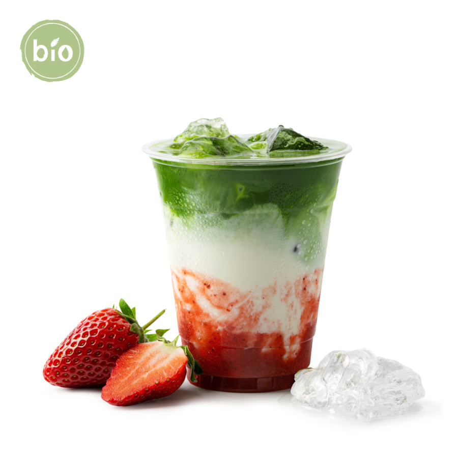 Ein Plastikbecher, gefüllt mit einer geschichteten Bio-Sommergeränke aus Grün, Weiß und Rot, gekrönt mit Eiswürfeln, steht neben ganzen und geschnittenen Erdbeeren und losem Eis. Ein grünes, rundes Bio-Etikett erscheint in der oberen linken Ecke.