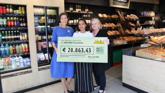 Drei Frauen stehen vor mit Lebensmitteln gefüllten Regalen und halten ein Schild mit der Aufschrift € 28.863,43 Ihre Spende unterstützt die WE & ME Foundation.