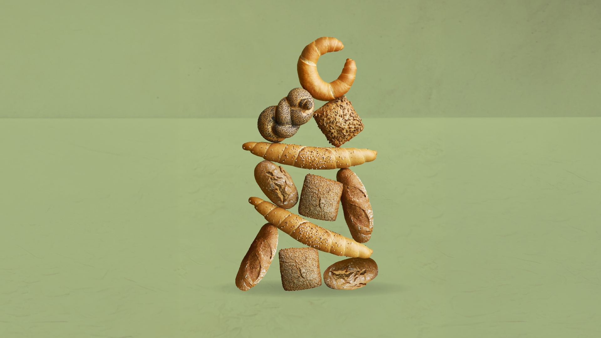 Verschiedene Brotsorten sind kunstvoll auf einer grünen Unterlage gestapelt und bilden die Silhouette einer Person.