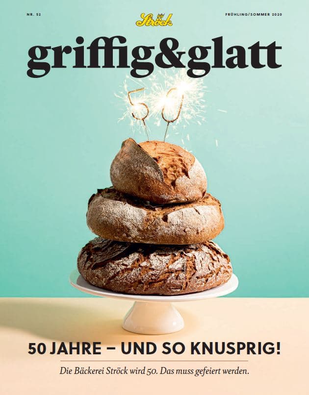 Drei übereinander gestapelte runde Brotlaibe mit Wunderkerzen obenauf, auf hellblauem Hintergrund. Der Text darunter feiert das 50-jährige Bestehen der Bäckerei Ströck.